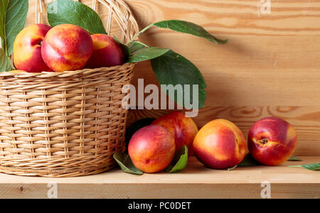 Les nectarines avec des feuilles dans un panier en osier sur une table en bois. Banque D'Images