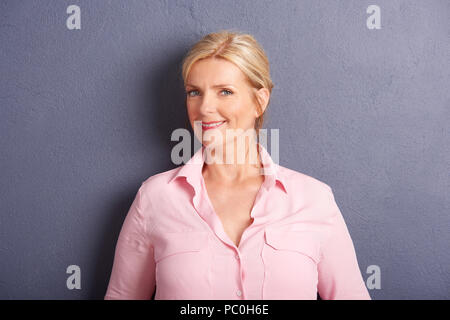 Cropped shot de belle mature woman looking at camera et souriant tout en se tenant au mur gris. Banque D'Images