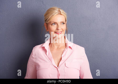 Cropped shot de belle mature woman sitting and smiling while standing au mur gris. Banque D'Images