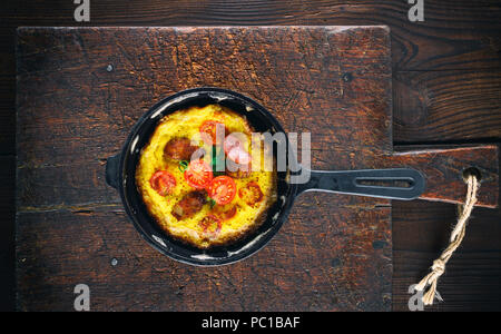 Poulet frit oeufs dans une ronde noire fonte poêle sur une vieille planche à découper en bois brun, vue du dessus Banque D'Images