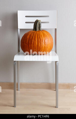 Grand orange citrouille sur une chaise moderne blanc sur fond de mur gris, l'automne et l'halloween décoration Banque D'Images