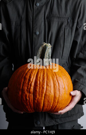 Man holding large orange citrouille en mains, vue en gros plan. L'automne et de Thanksgiving concept. Banque D'Images