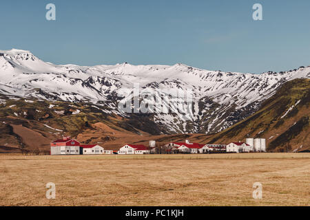 Paysage islandais typique de maisons blanches aux toits rouges contre montagnes dans petit village dans le sud de l'Islande. Banque D'Images