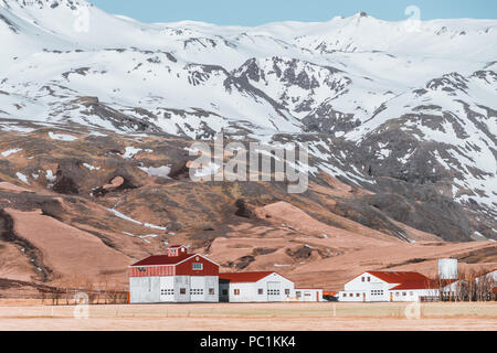 Paysage islandais typique de maisons blanches aux toits rouges contre montagnes dans petit village dans le sud de l'Islande. Banque D'Images