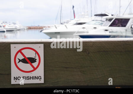 Pas de panneau d'avertissement de pêche sur banc en bois bloc pour assis dans pier avec des bateaux dans le port en arrière-plan Banque D'Images