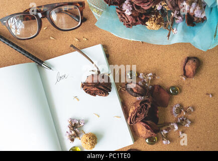 Vue supérieure de la couche plate witerd old rusty brown roses et l'amour mot sur blank white book avec lunettes floues et fleur bouquet bleu en arrière-plan sur crok Banque D'Images