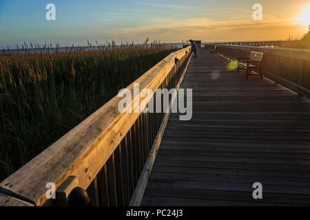 Une forte lumière au coucher du soleil au bord de scène illumine le ciel, nuages, Currituck Sound, et de premier plan de la promenade, deux personnes se pencha sur la rampe, canard, NC Banque D'Images