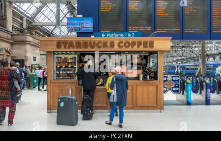 Baristas et clients au café Starbucks à la gare centrale de Glasgow. Les passagers en attente pour le train. Conseil des départs. Barrières de billets. Banque D'Images
