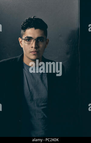 Studio portrait d'un homme âgé de 19 ans, le port de lunettes de lecture, un t-shirt et une veste noire Banque D'Images