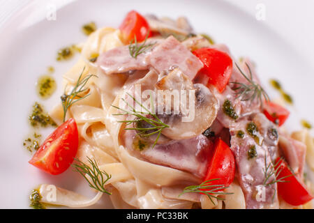 Tagliatelle aux champignons . Les pâtes italiennes sur plaque blanche avec champignons, jambon et tomate Banque D'Images