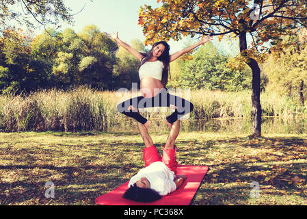 Jeune couple doing yoga acro. Femme enceinte au-dessus de son homme en souriant. Selective focus Banque D'Images