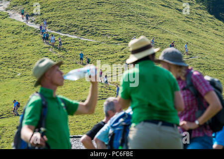 Hausham, Allemagne. 06Th Aug 2018. Les participants de l'ascension de l'alpage alpage management association de Haute-bavière à pied sur un sentier à l'Baumgartenalm, tandis qu'au premier plan un participant boissons quelque chose. En raison de la persistance de la chaleur, cette année, moins de personnes ont pris part à l'assemblée annuelle de l'inspection principale de l'alpage alpage management association. Credit : Lino Mirgeler/dpa/Alamy Live News Banque D'Images