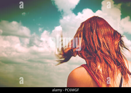 Anonymous femme aux cheveux rouges et bleu ciel.femme sur son dos avec ses cheveux déplacé par l'air à la recherche à l'infini Banque D'Images