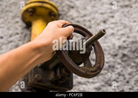 Man holding old weathered grue de gaz sur l'arrière-plan d'un mur gris. L'ancien gaz porte de couleur jaune est sur un tuyau et bloque un tuyau. Le pipeline avec des grues pour donner du gaz sur le mur. Banque D'Images