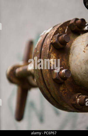 Old weathered grue et de gaz d'échappement sur l'arrière-plan d'un mur gris. L'ancien gaz porte de couleur jaune est sur un tuyau et bloque un tuyau. Le pipeline avec des grues pour donner du gaz sur le mur. Banque D'Images