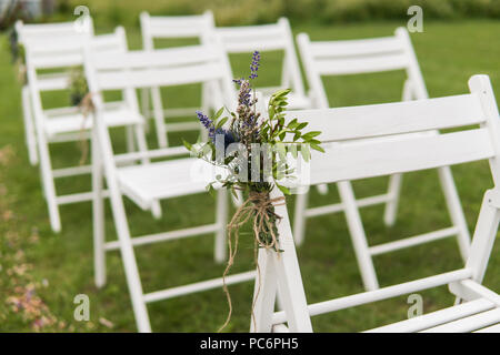 Chaises de mariage blanc décoré de fleurs fraîches sur une herbe verte. Chaises en bois vides pour les hôtes en pelouse verte dans le jardin préparé pour la cérémonie du mariage. Banque D'Images
