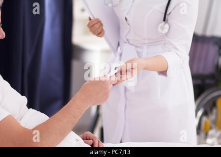 Infirmière en donnant son patient thermomètre. Photo de la remise au lit du patient de thermomètre pour mesurer sa température. Banque D'Images