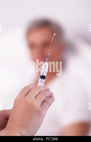 Nurse holding injection dans ses mains. Close up shot of female doctors hands holding syringe. Trouble du patient en arrière-plan. Banque D'Images