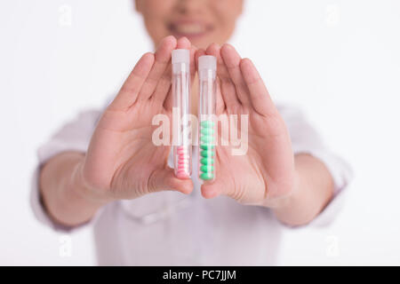 Female doctor holding des bouteilles de pilules à proximité de l'appareil photo. Close up shot of female nurse montrant deux tubes avec un peu de vert et rose comprimés médecine. Banque D'Images