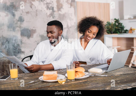 African American man le petit-déjeuner avec petite amie faire les achats en ligne dans la cuisine Banque D'Images