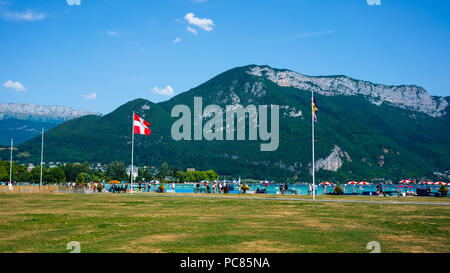 Les gens autour du lac d'Annecy rive avec Savoie drapeau région et Veyrier mont des Alpes montagnes en arrière-plan Banque D'Images