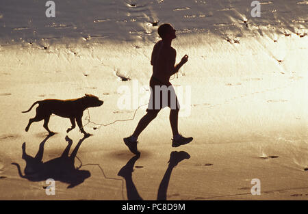 Un homme jogging le Sands Beach avec son chien. Banque D'Images
