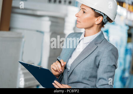 Femme inspecteur dans la rédaction de notes sur casque clipboard in warehouse Banque D'Images