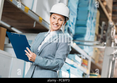 Femme inspecteur dans la rédaction de notes sur casque clipboard in warehouse Banque D'Images