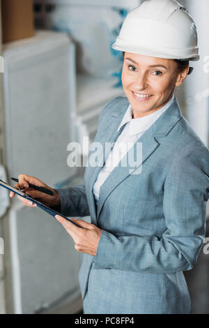 Femme inspecteur dans la rédaction de notes sur casque clipboard in warehouse Banque D'Images