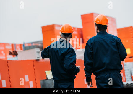 Vue arrière de deux constructeurs de casques bleus qui travaillent à l'extérieur sur la construction Banque D'Images