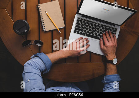 Vue aérienne de l'homme à l'aide d'ordinateur portable avec le site web de google tout en étant assis à table avec le café et le bloc-notes Banque D'Images