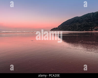 Vue paysage de montagne à partir de Manzanita Neahkahnie Beach sur la côte Pacifique du nord de l'Oregon. Joli ciel rose réfléchissant sur le sable humide. Banque D'Images