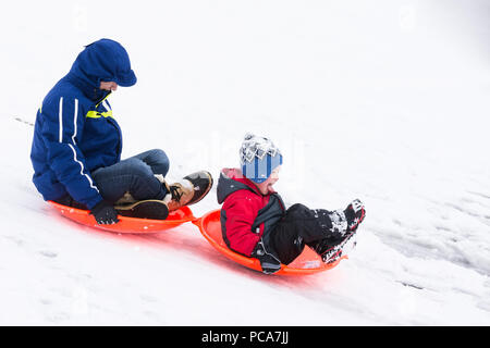 Un homme âgé et un jeune garçon de la luge sur une colline enneigée en traîneaux orange vif Banque D'Images