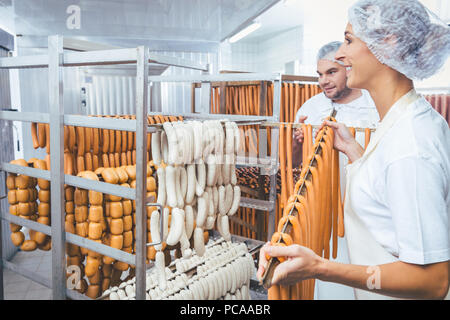 Femme travaillant dans une boucherie mettre les saucisses sur faisceau en rack Banque D'Images