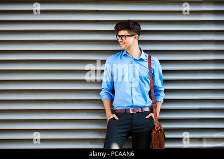Bureau souriant homme debout contre un mur, après le travail abstrait avec sac en cuir, attendant quelque chose ou quelqu'un Banque D'Images