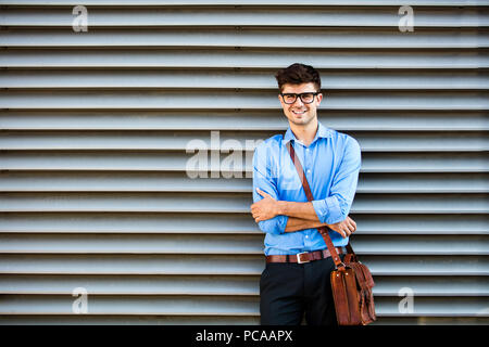 Jeune homme de bureau contre un mur en attente de quelque chose ou quelqu'un, dans la tenue et le sac de cuir de bureau, debout contre un mur en attente de somene avec fo Banque D'Images