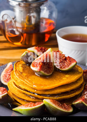 Pile de crêpes à la citrouille avec des figues et du miel et du thé chaud. Arrière-plan de l'alimentation de l'automne sur fond gris bleu Banque D'Images