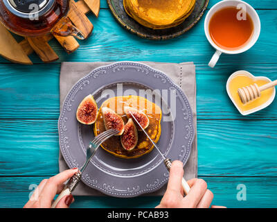 Manger des crêpes à la citrouille avec des figues et du miel avec du thé chaud. Automne fond alimentaire sur table en bois vert. Woman's hands Banque D'Images