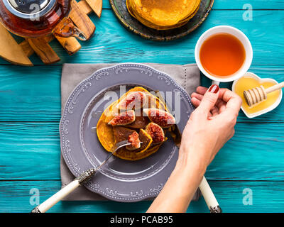 Manger des crêpes à la citrouille avec des figues et du miel avec du thé chaud. Automne fond alimentaire sur table en bois vert. Woman's hands Banque D'Images