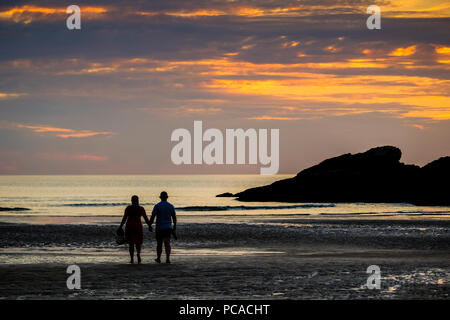 Couple sur la plage de Porth Newquay en Cornouailles, en regardant la mer au coucher du soleil Banque D'Images