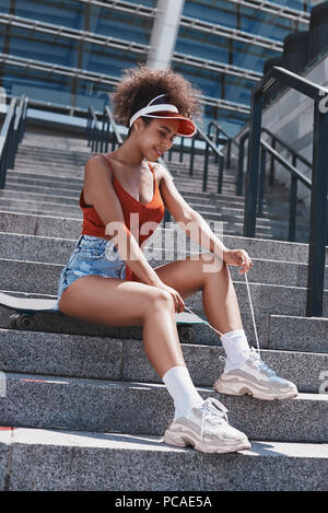 Jeune femme en style libre de pare-soleil dans la rue assis sur des escaliers Banque D'Images