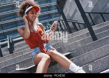 Jeune femme en style libre de pare-soleil dans la rue assis sur des escaliers Banque D'Images