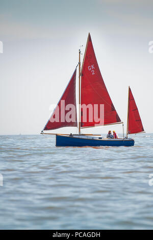 Un voilier rouge vu sur mer calme sur une chaude journée ensoleillée avec ciel bleu. Banque D'Images