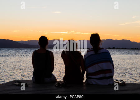 Les gens sur le dos regardant le coucher du soleil sur la plage Banque D'Images