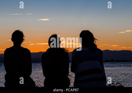 Les gens sur le dos regardant le coucher du soleil sur la plage Banque D'Images