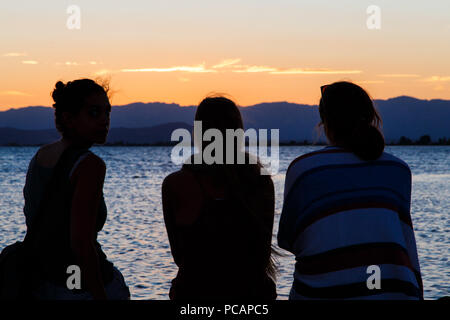 Les gens sur le dos regardant le coucher du soleil sur la plage Banque D'Images