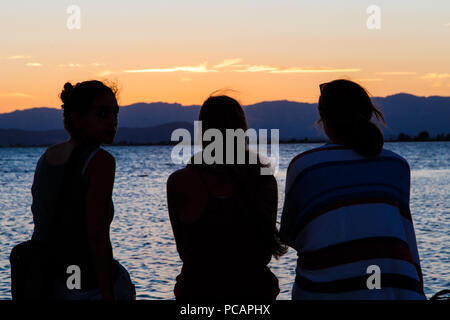 Les gens sur le dos regardant le coucher du soleil sur la plage Banque D'Images