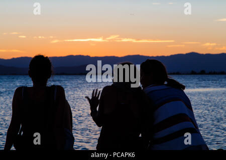 Les gens sur le dos regardant le coucher du soleil sur la plage Banque D'Images