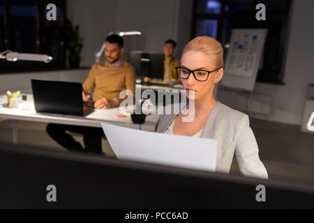 Businesswoman avec papiers travaillant au bureau de nuit Banque D'Images