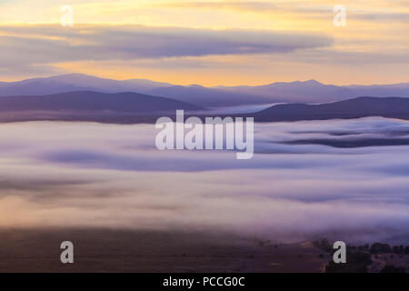 Les nuages bas couvrant des pics de montagne au coucher du soleil Banque D'Images